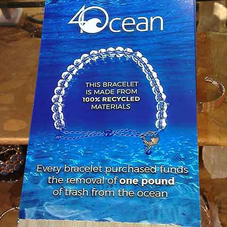 A promotional tag for a 4Ocean Bracelet Blue Signature, made from 100% recycled materials, highlighting that each purchase funds the removal of one pound of ocean trash.