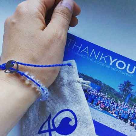 A hand holding a &quot;thank you&quot; card with an ocean conservation theme, accompanied by a 4Ocean Bracelet Blue Signature, symbolic of support for marine life protection and made from recycled materials and ocean trash removal efforts.