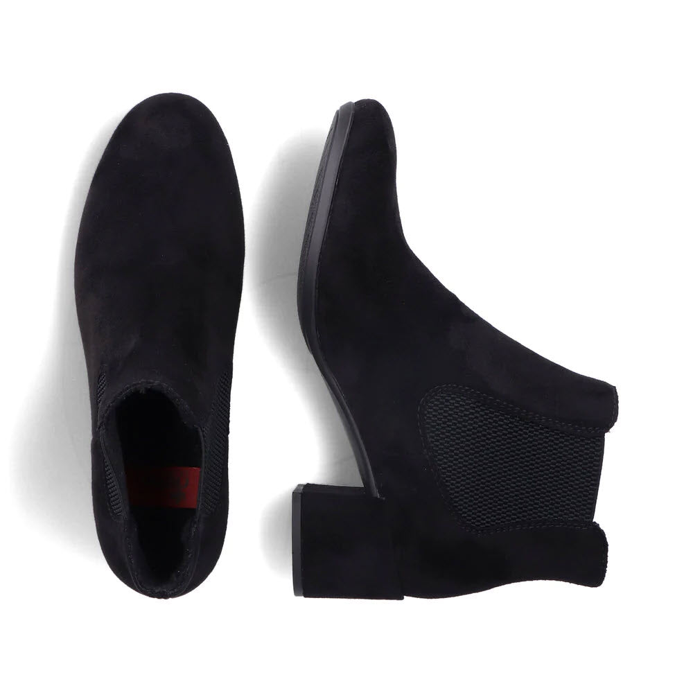 A pair of black suede Chelsea boots, one laying flat and the other standing upright with visible elastic side panels and block heels, features the sleek style of Rieker RIEKER BLOCK HEEL DRESS BOOTIE BLACK STRETCH - WOMENS.