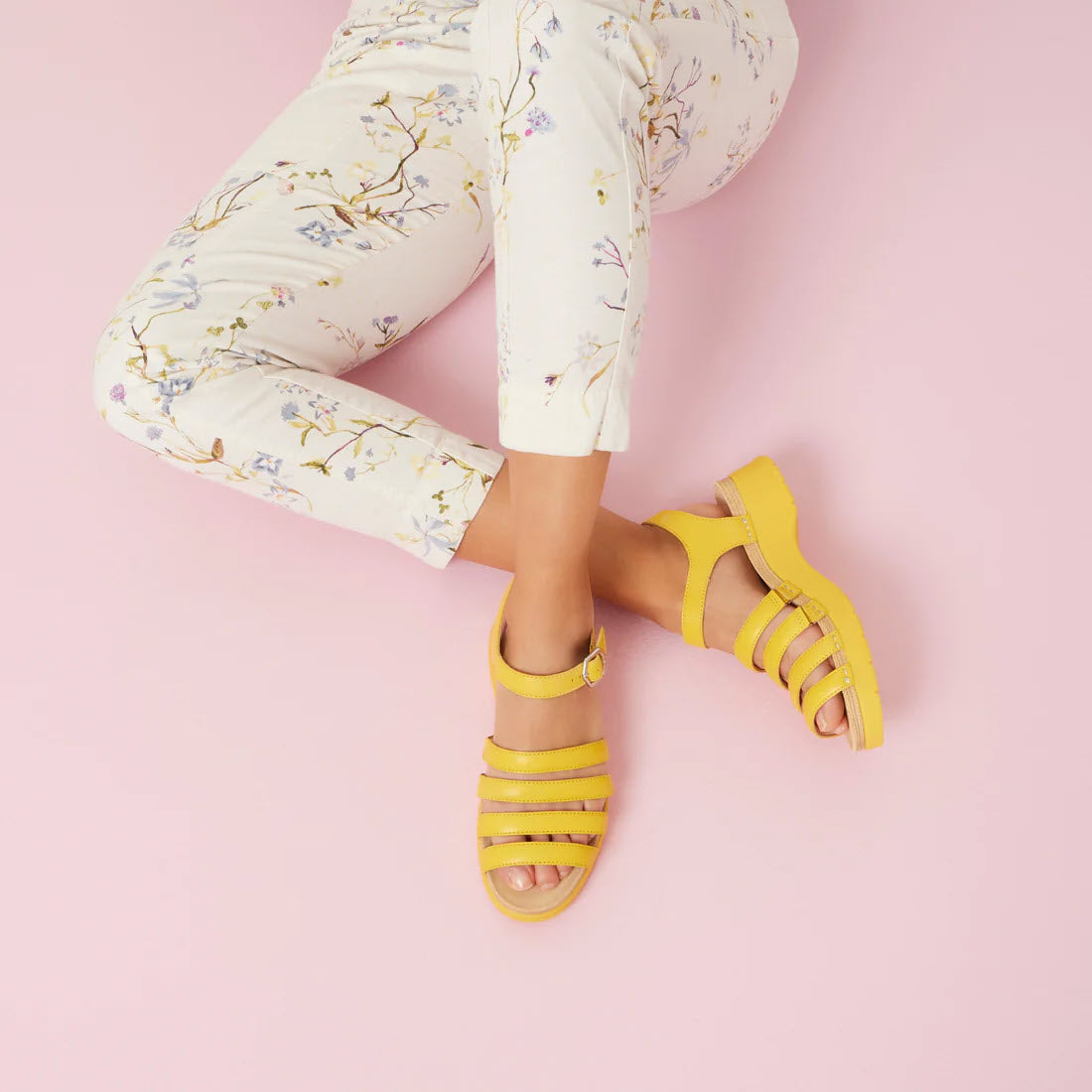 Person wearing Dansko Roxie Yellow sandals with straps and floral pants against a pink background.