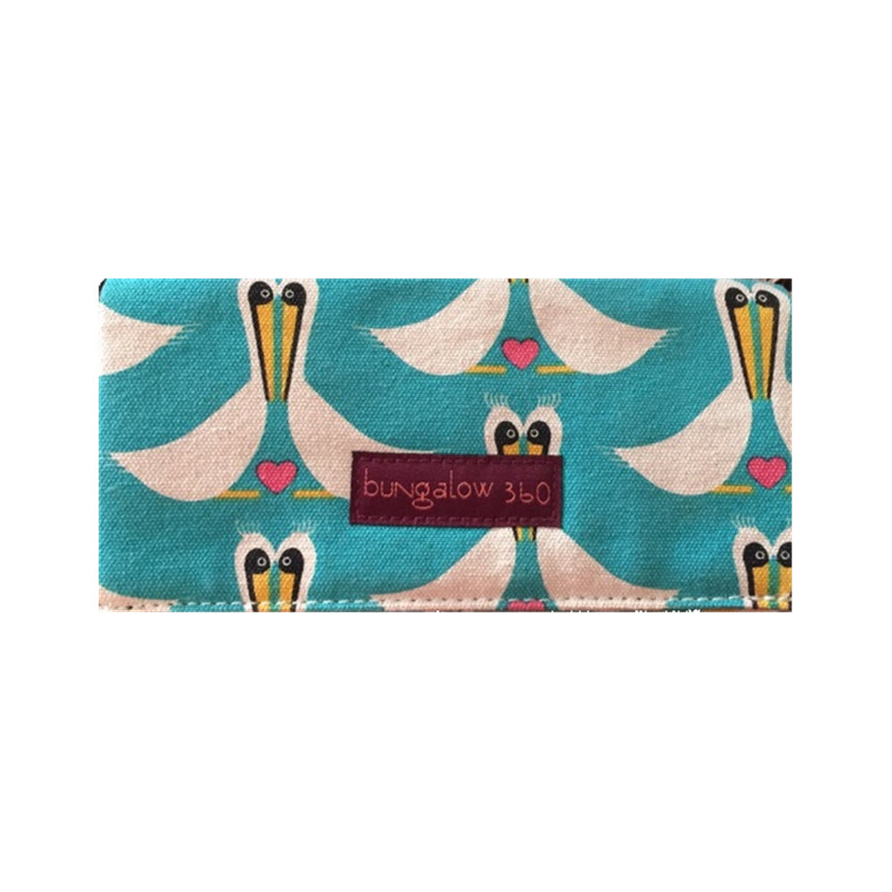 Rectangular fabric clutch featuring unique designs of pelican illustrations in pastel tones and a label reading "Bungalow 360 ZIP AROUND WALLET PELICAN" by Bungalow 360.