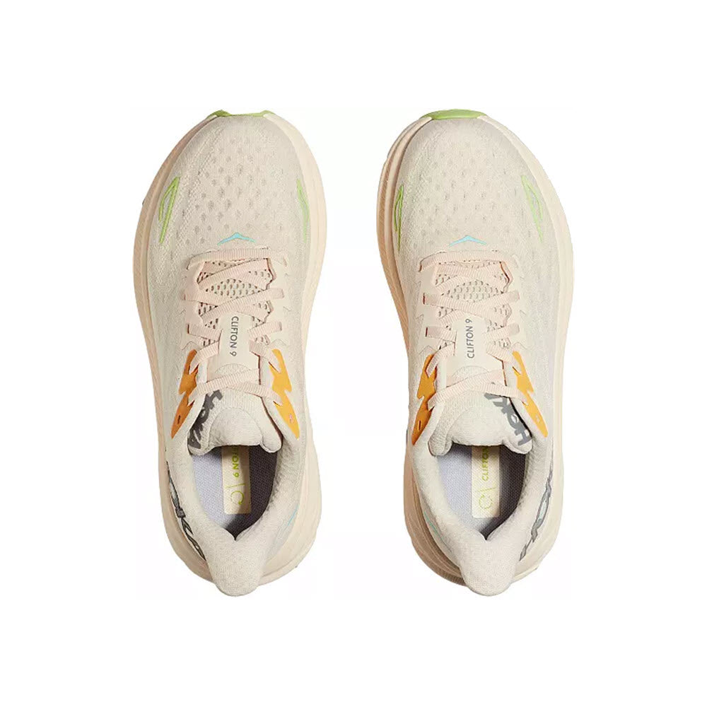 Top view of a pair of light-colored Hoka CLIFTON 9 VANILLA/ASTRAL - WOMENS running shoes with orange and green accents, isolated on a white background.