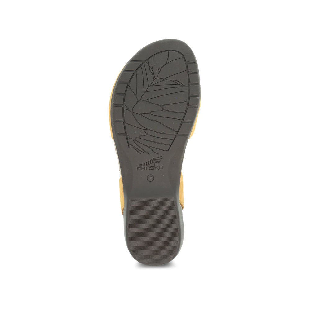 A close-up image of the sole of a Dansko ROWAN MUSTARD - WOMENS summer sandal, featuring intricate leaf patterns and the brand&#39;s logo.