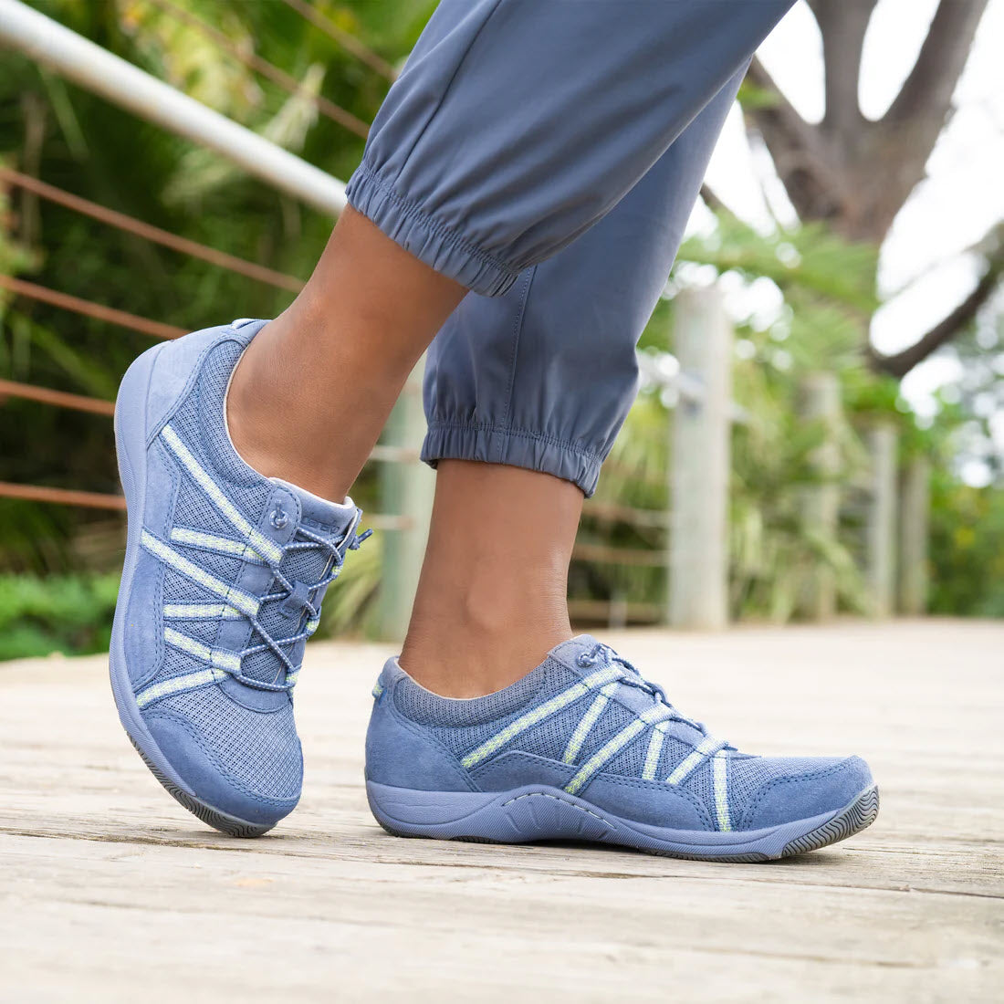 Close-up of a person&#39;s feet wearing Dansko Harlyn Blue - Womens premium support, lightweight performance sneakers on a wooden boardwalk.