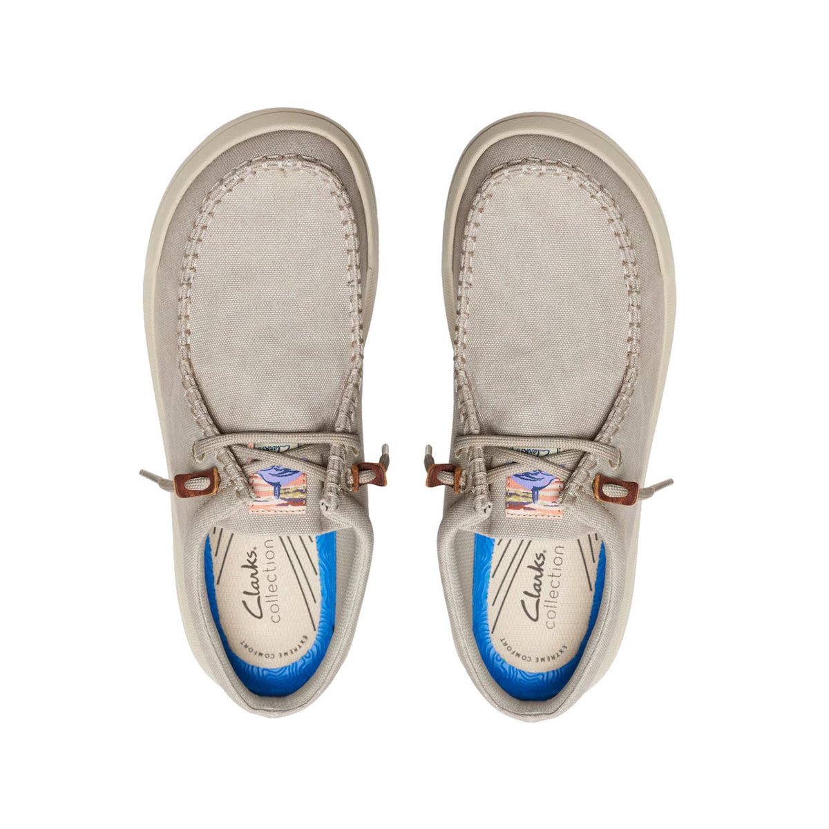 A pair of Clarks Driftlite Surf Slip On Moc light gray canvas slip-on shoes with brown leather accents and blue insoles, viewed from above on a white background.