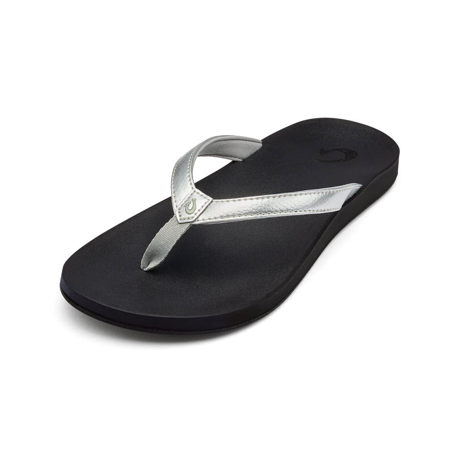 A single black flip-flop with a metallic silver thong strap on a white background, perfect as water-friendly footwear. Try the OLUKAI PUAWE SILVER - WOMENS from Olukai.