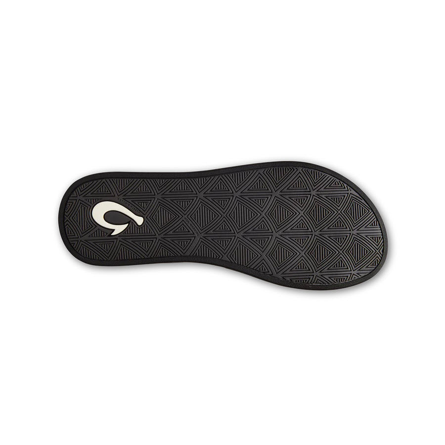 A black Olukai Puawe Silver sandal sole featuring a geometric pattern and a white logo resembling a stylized letter &quot;q&quot; in the center on a white background.