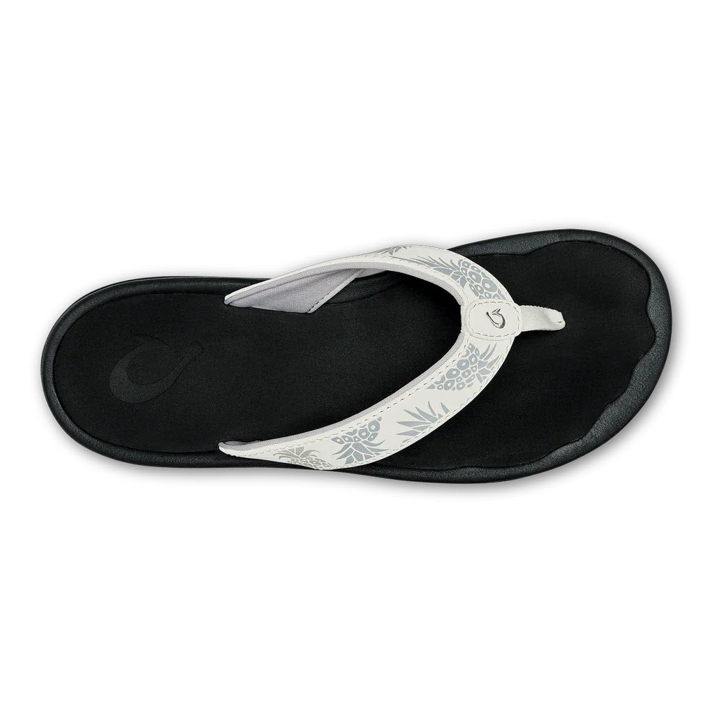 A single OLUKAI OHANA BRIGHT WHITE - WOMENS flip-flop with a black sole and a white patterned strap on a white background.