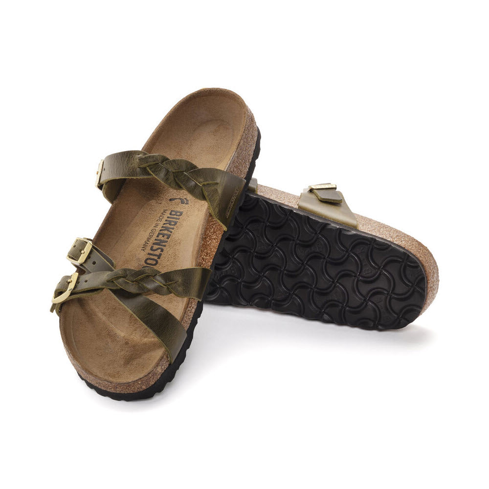 A pair of Birkenstock sandals with olive green straps and buckles, cork-latex footbeds, and black wavy soles, isolated on a white background.