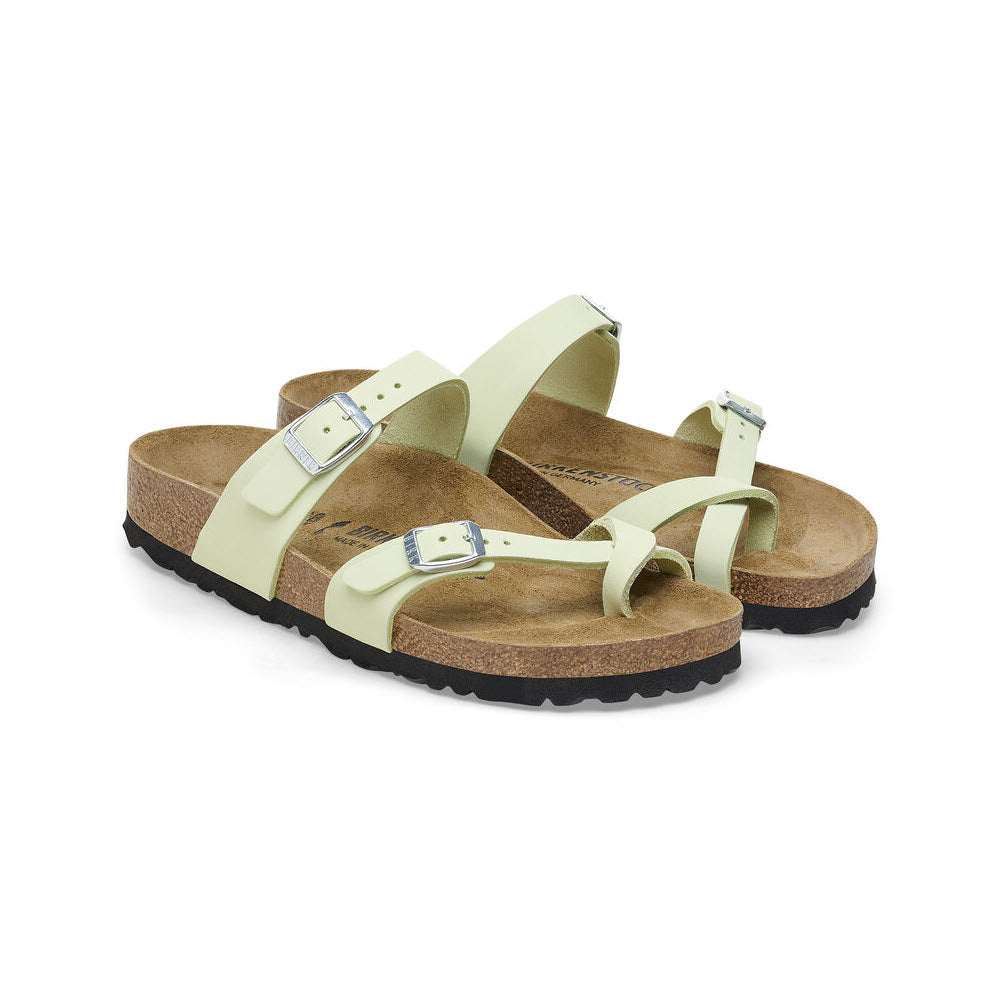 A pair of light green Birkenstock Mayari sandals with adjustable buckled straps and cork soles, presented on a white background.