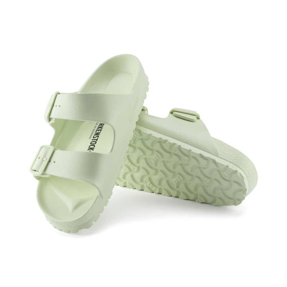 Pair of light green Birkenstock Arizona sandals with buckle straps and textured soles, displayed against a white background.