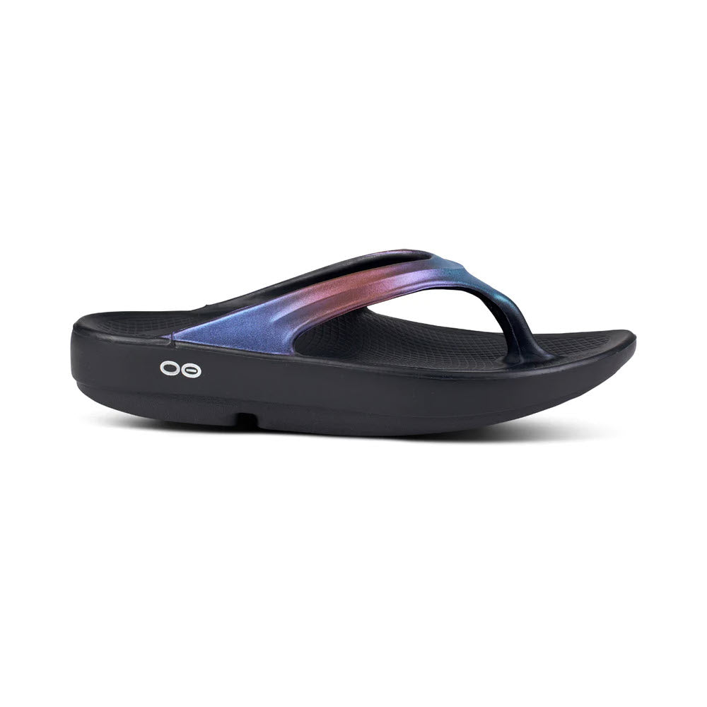 A moisture and bacteria-resistant, Oofos OOlala Luxe Midnight Spectre - Women's flip-flop-styled sandal with a glossy, multicolored strap on a white background.