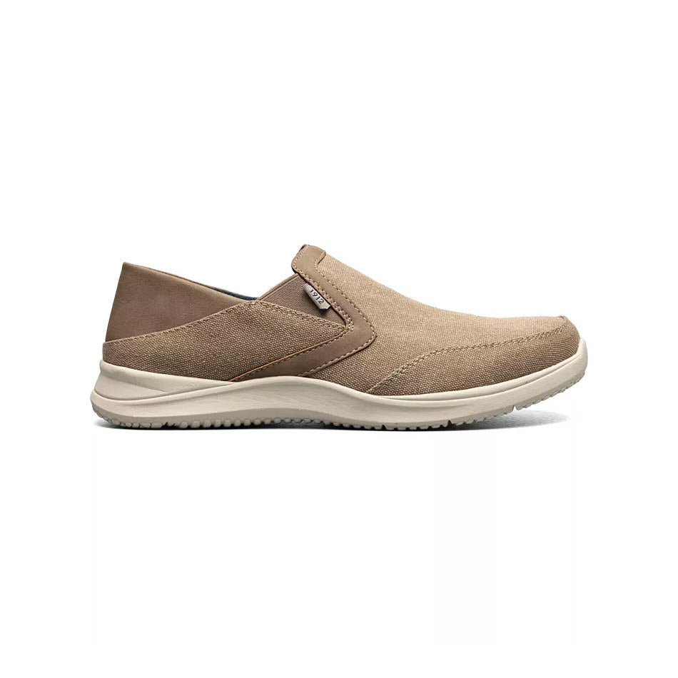 A single beige Nunn Bush Conway EZ canvas moc toe slip on stone with a brown accent and a white sole, viewed from the side on a white background.