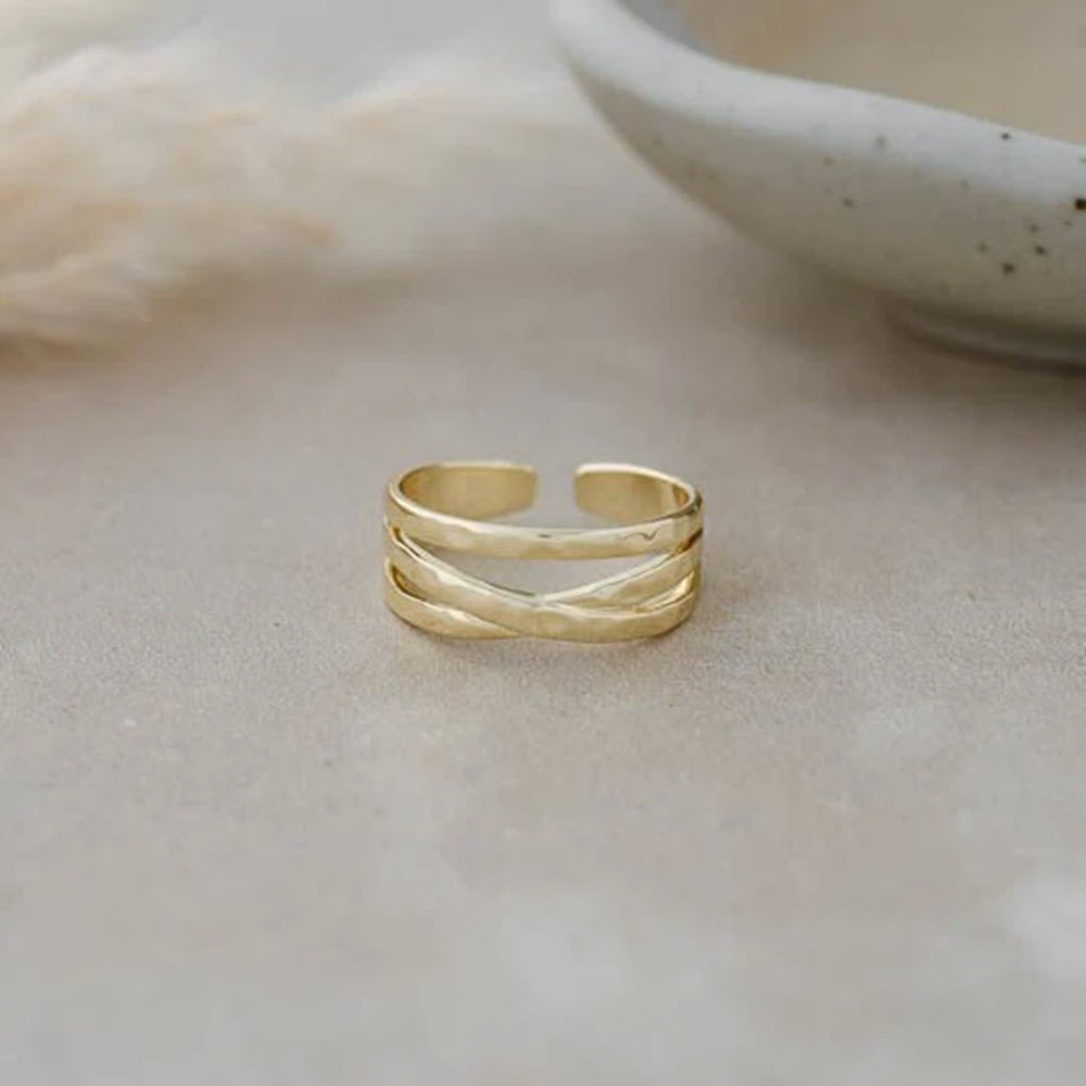 GLEE ILLUSION RING GOLD displayed on a light beige surface, with soft-focus background featuring neutral tones. This anti-tarnish piece ensures lasting beauty and durability.