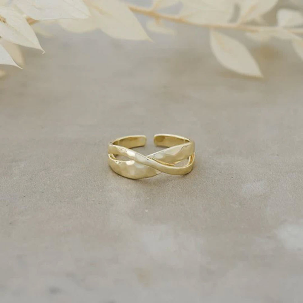 A Glee Ramona ring gold with anti-tarnish coating, displayed on a neutral textured surface with soft, pale leaves in the background.