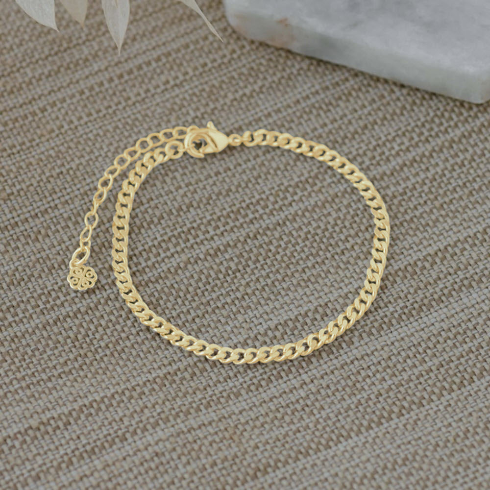 Glee Brazen bracelet gold on a textured surface with an extension chain and small charm, featuring hypoallergenic jewelry, set against a light gray background with marble and lace elements.