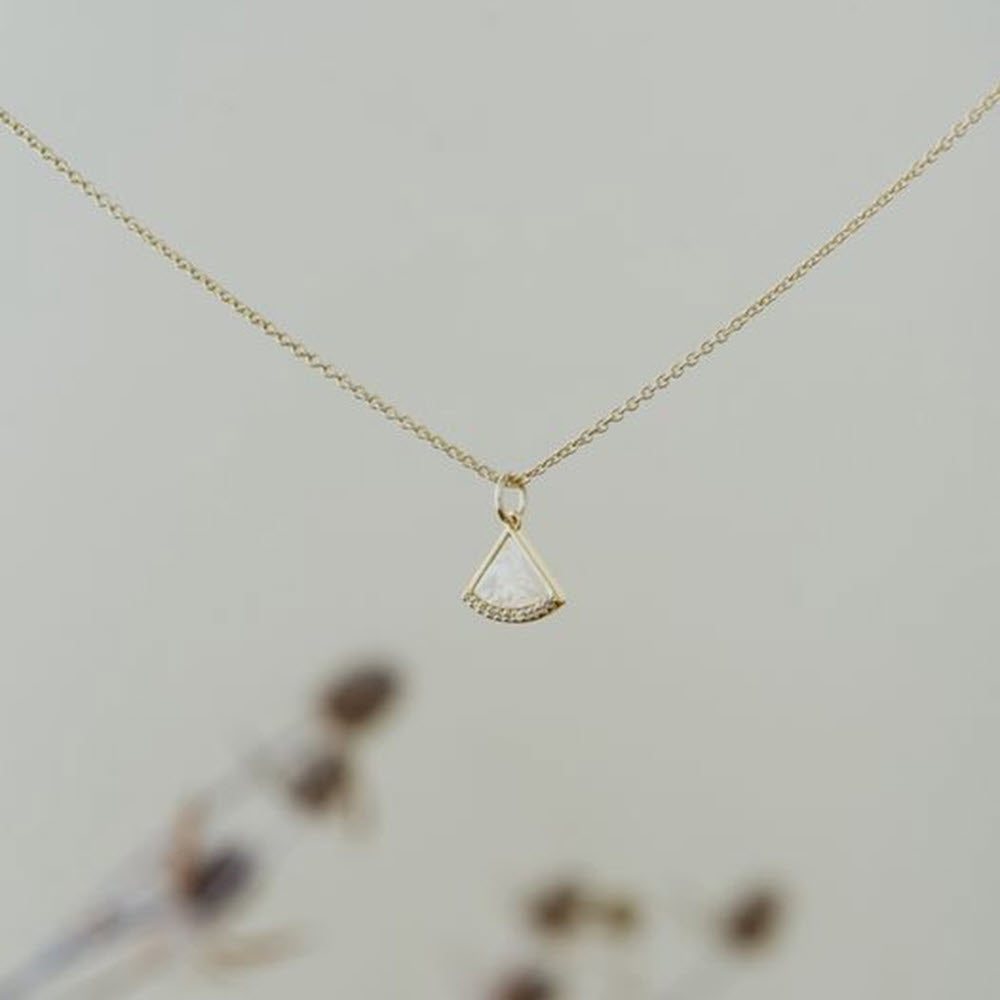 Glee Fanfare necklace with a small, triangular pendant set with diamonds, displayed against a blurred floral background. Now featuring a Victorian-style chain.