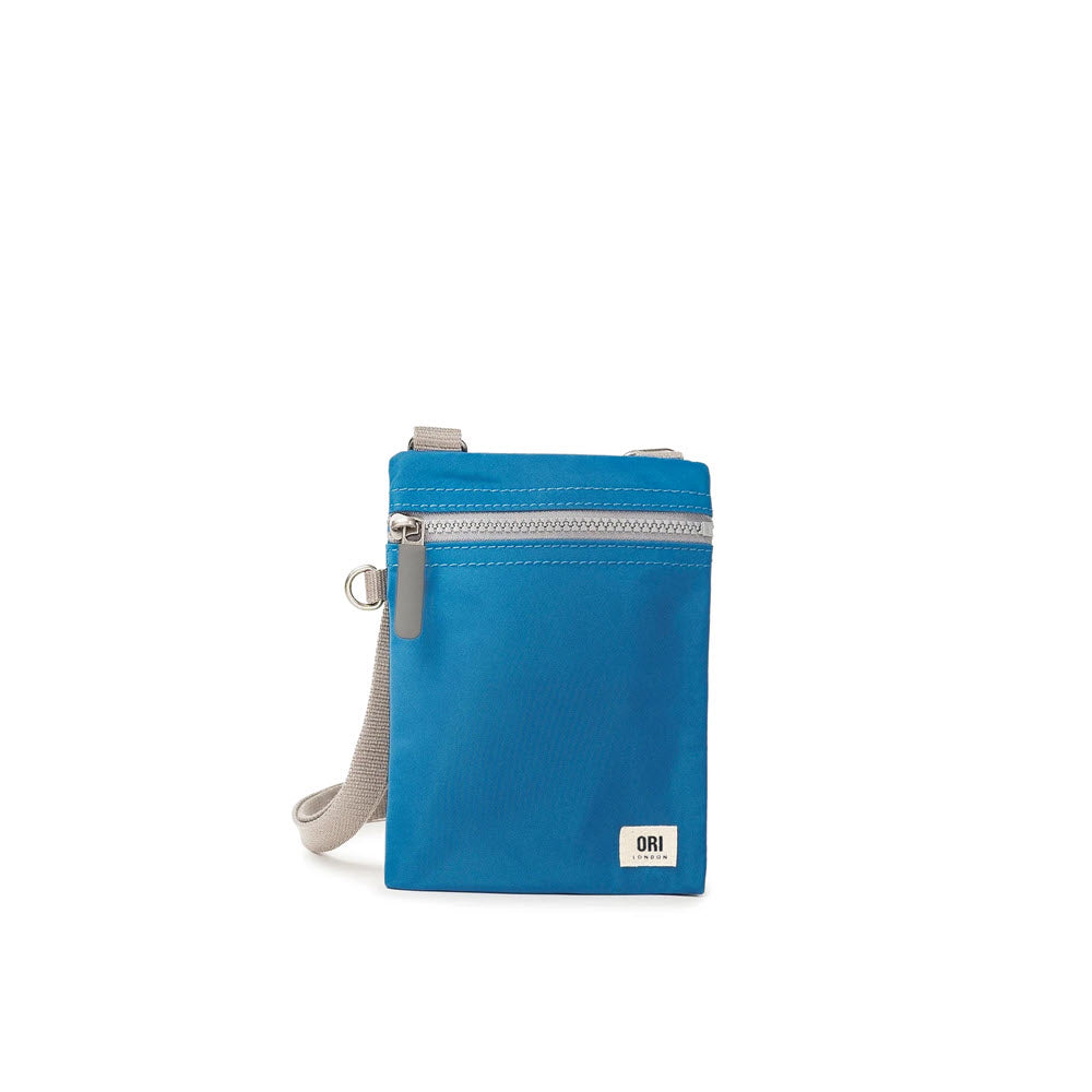 A blue ORI LONDON CHELSEA CROSSBODY SEAPORT with a front zipper pocket and a gray strap, isolated on a white background.