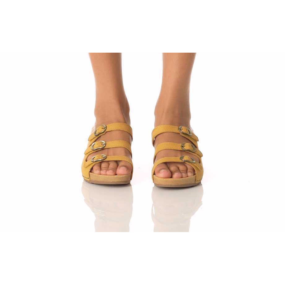 A pair of feet donning Dansko Tarin Yellow Burnished Nubuck sandals with adjustable forefoot straps against a white background.