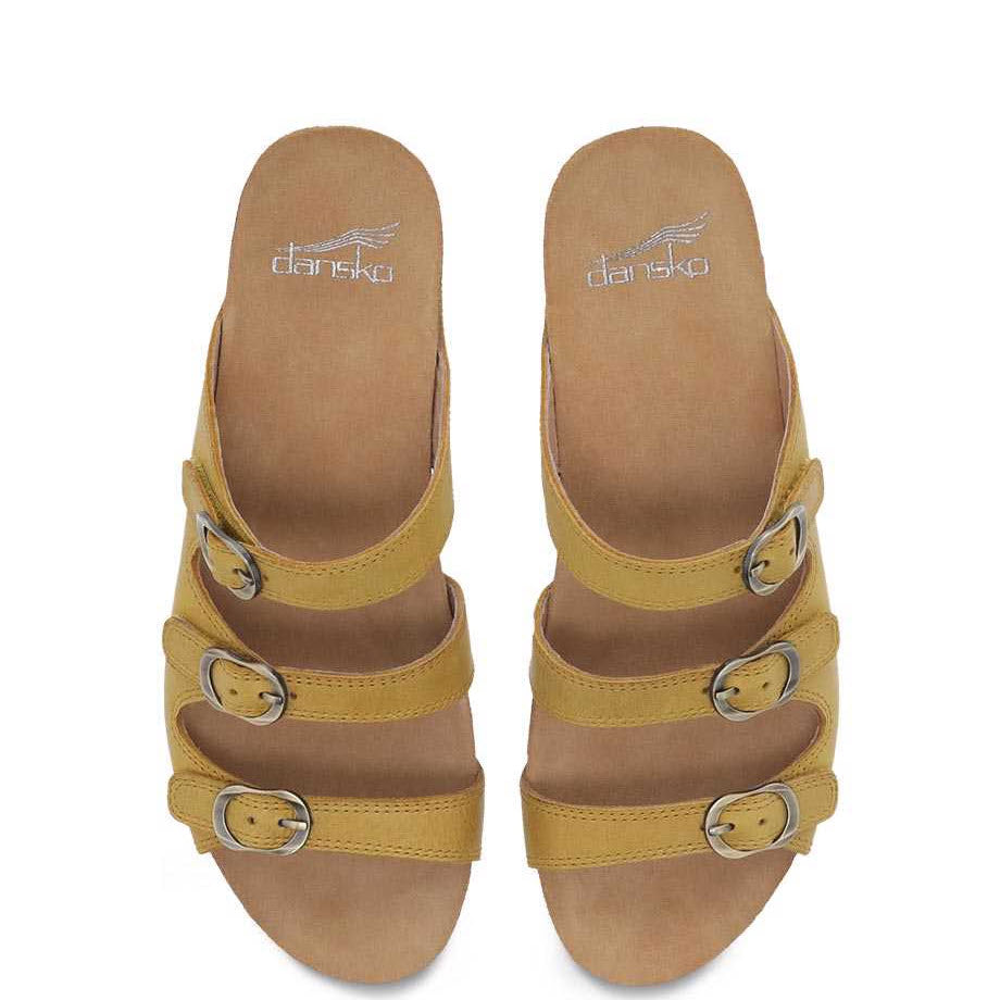 A pair of Dansko Tarin Yellow Burnished Nubuck wedge slide sandals with adjustable forefoot straps and buckle details.