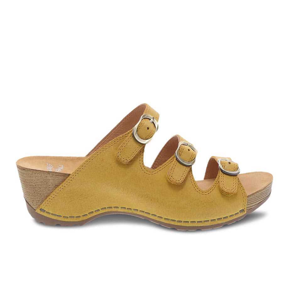 A single tan-colored, Dansko Tarin Yellow Burnished Nubuck wedge sandal with adjustable forefoot straps displayed against a white background.