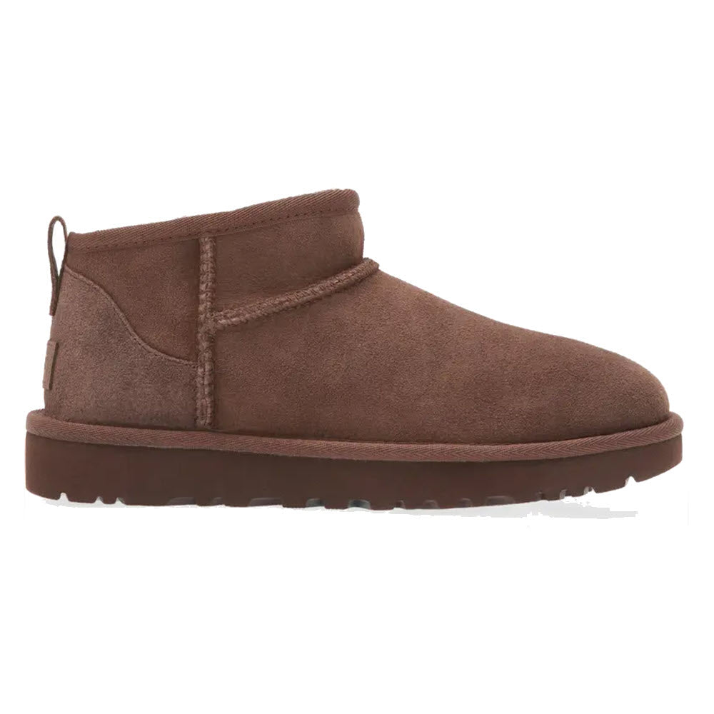 A side view of a brown suede Ugg Classic Ultra Mini Burnt Cedar boot with a flat sole and an ultra-short shaft.