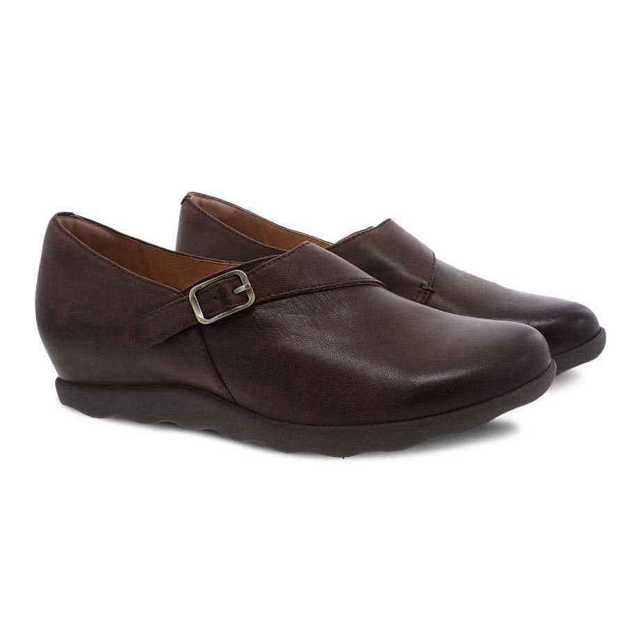 A pair of Dansko Marisa brown burnished leather loafers with leather uppers and a buckle detail on a white background.