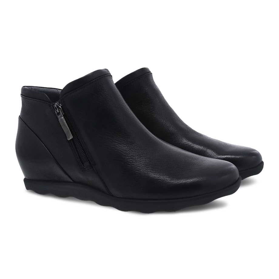 A pair of Dansko Miki black burnished nubuck leather wedge ankle boots with side zippers, isolated on a white background.