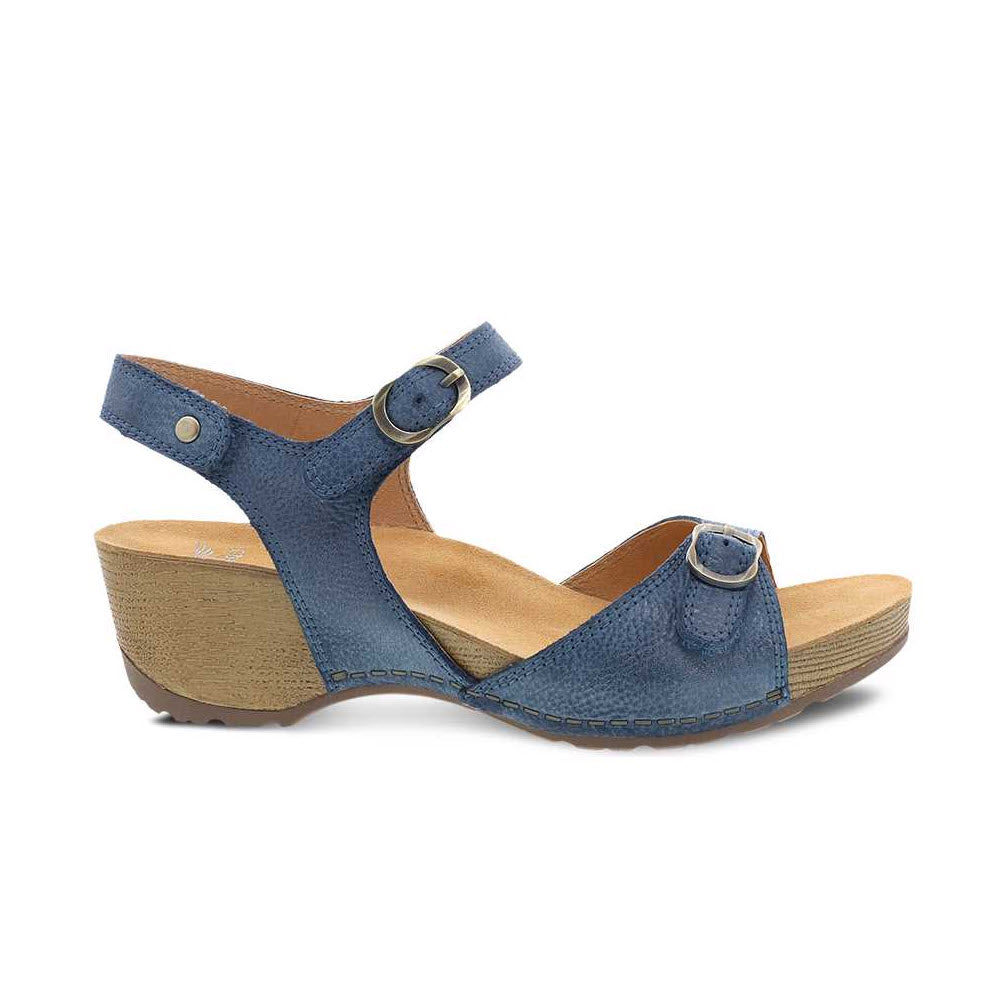 A pair of Dansko Tricia Blue women's leather sandals with adjustable straps and a low cork wedge heel, featuring a memory foam footbed, isolated on a white background.