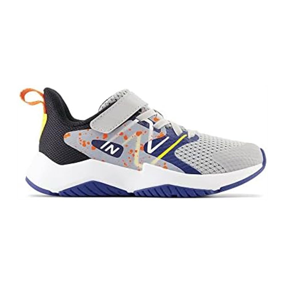 Side view of a gray New Balance Rave Run v2 Rain Cloud kids’ running shoe with white, orange, and blue accents, featuring a velcro strap and a thick blue sole.