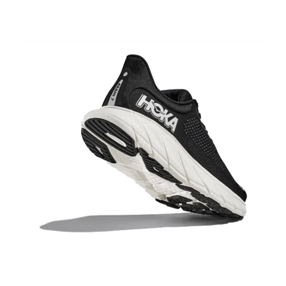A black and white HOKA ARAHI 7 running shoe suspended in air against a white background.