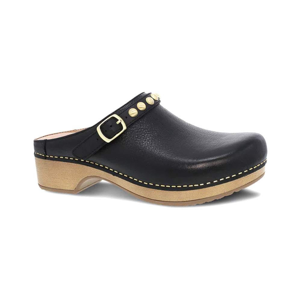 Dansko Britton black leather mule with a buckle, wooden sole, and yellow stitching, isolated on a white background.