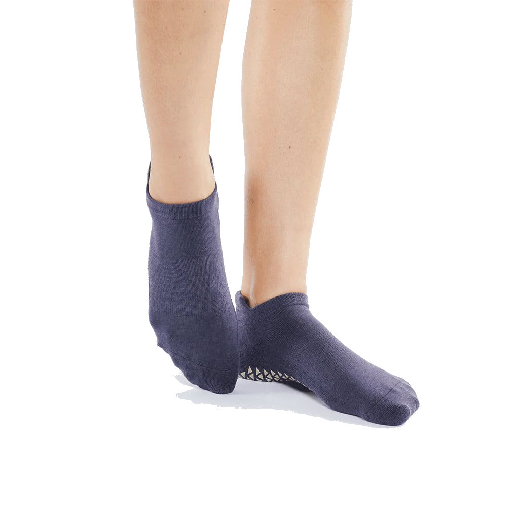 A person wearing dark blue Pointe Studio Union Low Grip Socks Amethyst, designed for barre and pilates, standing against a white background.