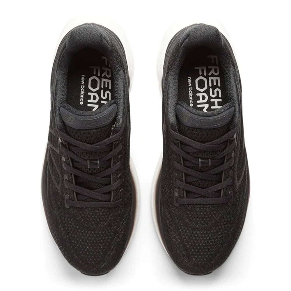 Top view of a pair of black runners with white soles, labeled &quot;NEW BALANCE 1080K13 BLACK - WOMENS&quot; on the insole.