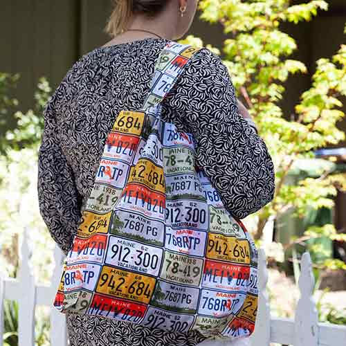 Woman standing outdoors wearing a jacket and carrying a BLU BAG MAINE LICENSE PLATE by Rockflowerpaper.