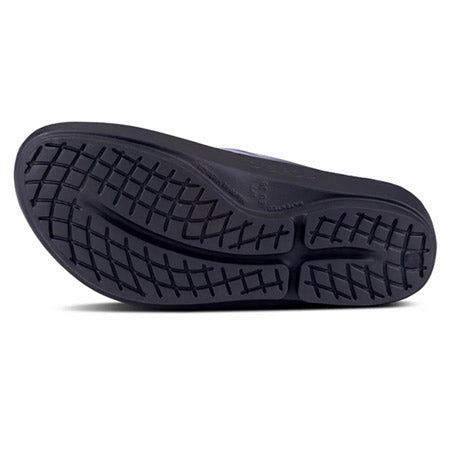 A close-up of a OOFOS OOLALA LUXE BLACK/ATLANTIS - WOMENS sandal sole with a waffle tread pattern, displayed against a white background.