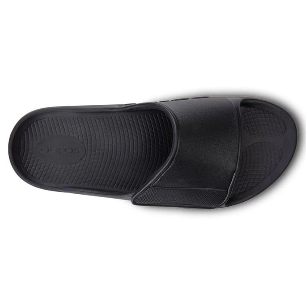 A single black Oofos slide sandal with a textured footbed and the logo embossed near the heel, viewed from above, featuring OOfoam technology.