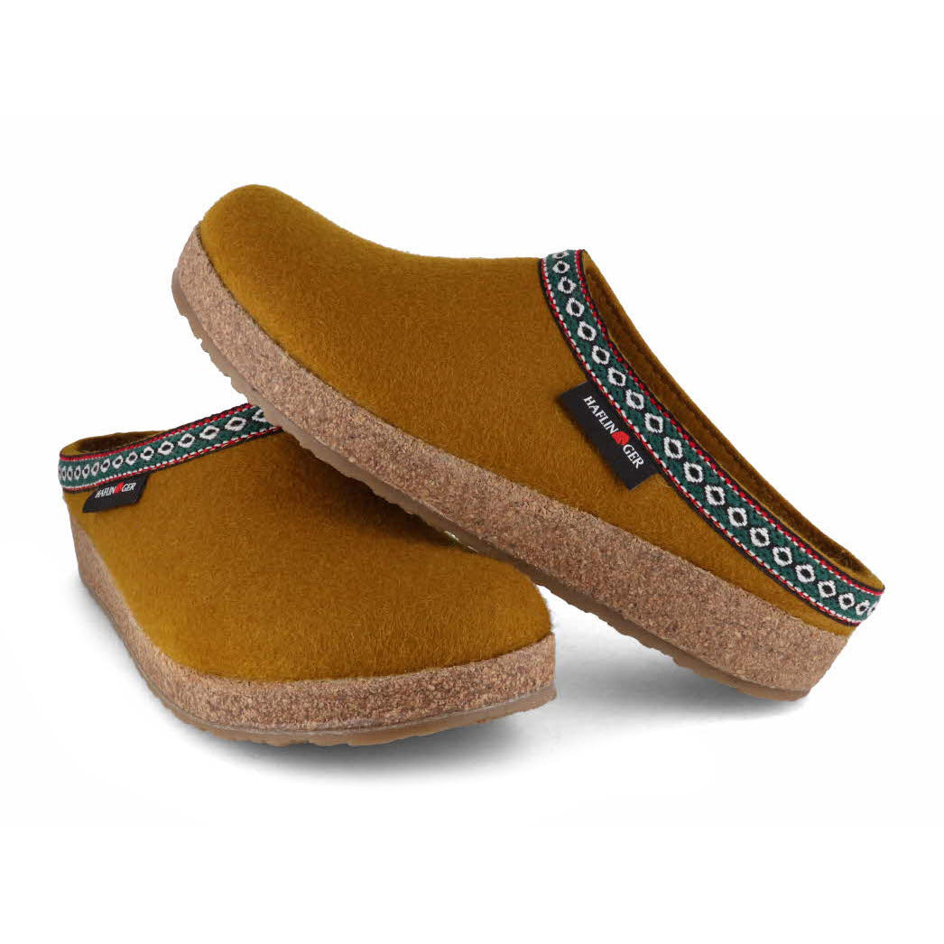 A pair of HAFLINGER GZ MUSTARD - WOMENS clog-style slippers featuring a virgin wool felt band around the upper edge, set against a white background.