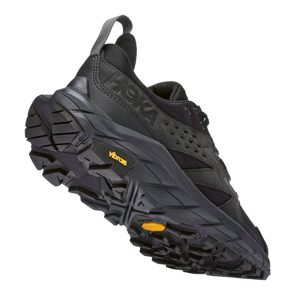 A black Hoka Anacapa Breeze Low trail running shoe with Vibram® Megagrip outsole, viewed from the side against a white background.