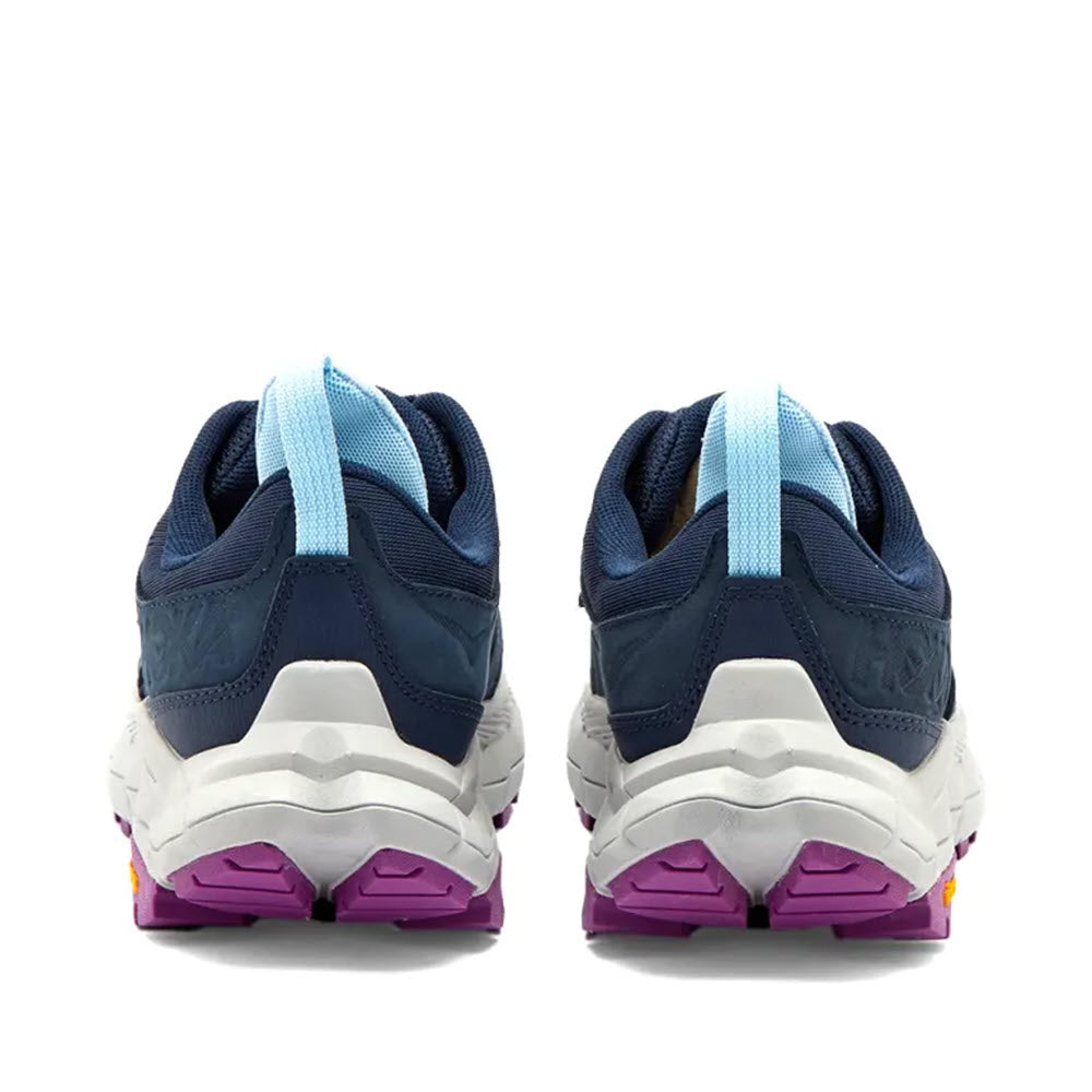 Rear view of a pair of HOKA ANACAPA BREEZE LOW OUTER SPACE/HARBOR MIST - WOMEN lightweight hiking shoes with white soles and purple accents, featuring a light blue pull tab on each heel.