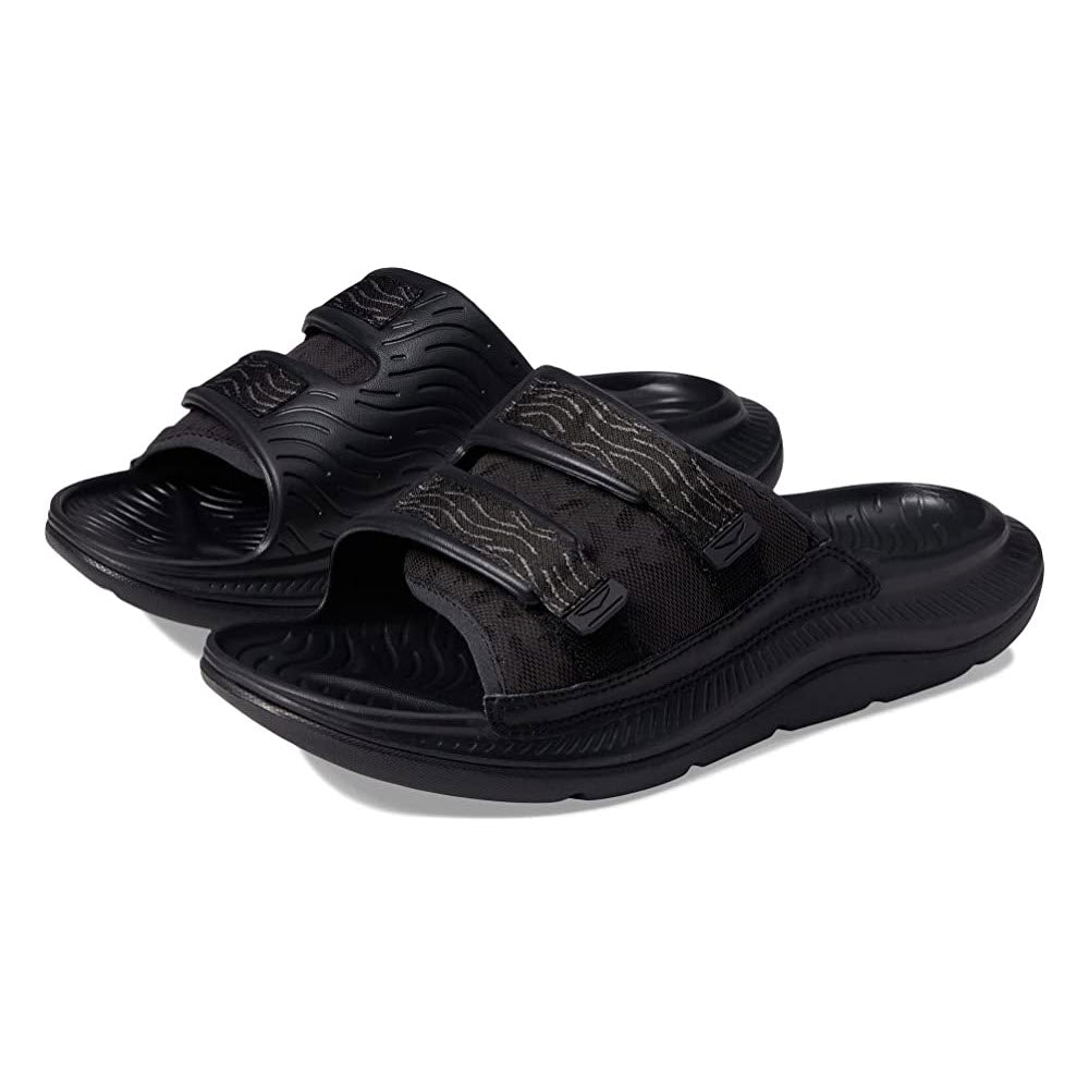 A pair of black, adjustable ORA LUXE BLACK/BLACK - ADULT strap sandals with textured insoles isolated on a white background.