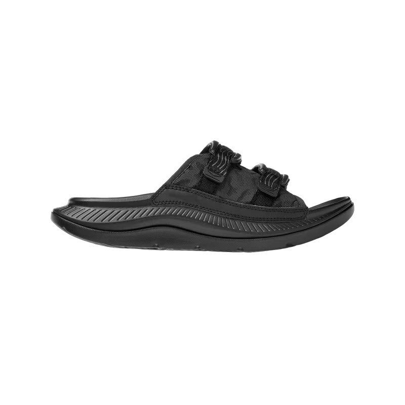 Black ORA LUXE BLACK/BLACK slide with a textured sole and adjustable Ariaprene® strap on a white background by Hoka.