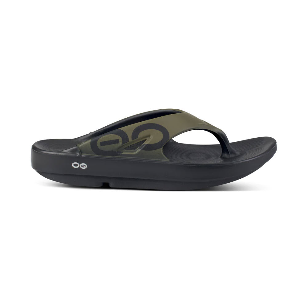 A single black sandal with a camo-patterned strap and a circular logo on the side, positioned on a plain white background. This Oofos OOriginal Sport Tactical Green - Mens features moisture-resistant properties.