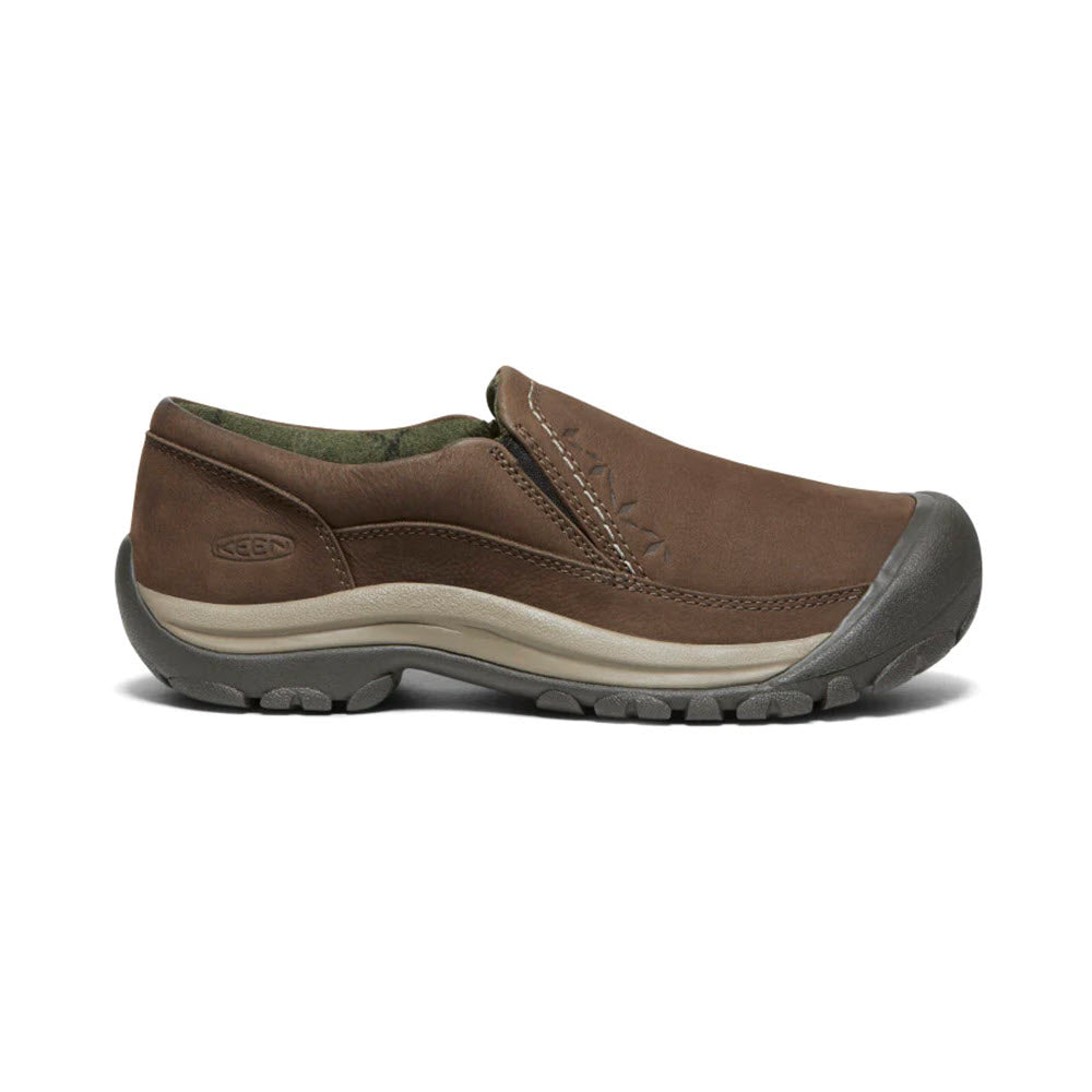 A brown KEEN KACI III WINTER DARK EARTH - WOMENS slip-on shoe with a rugged sole, branded with &quot;Keen&quot; on the side. The shoe features a reinforced toe, stitching details along the upper, and waterproofing to keep your feet dry in wet conditions.