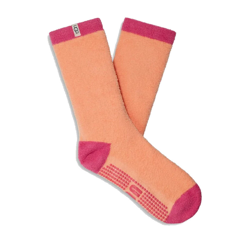A pair of UGG Paityn cozy gripper crew socks in coral pink with branded grips on the sole that enhance traction, isolated on a white background.