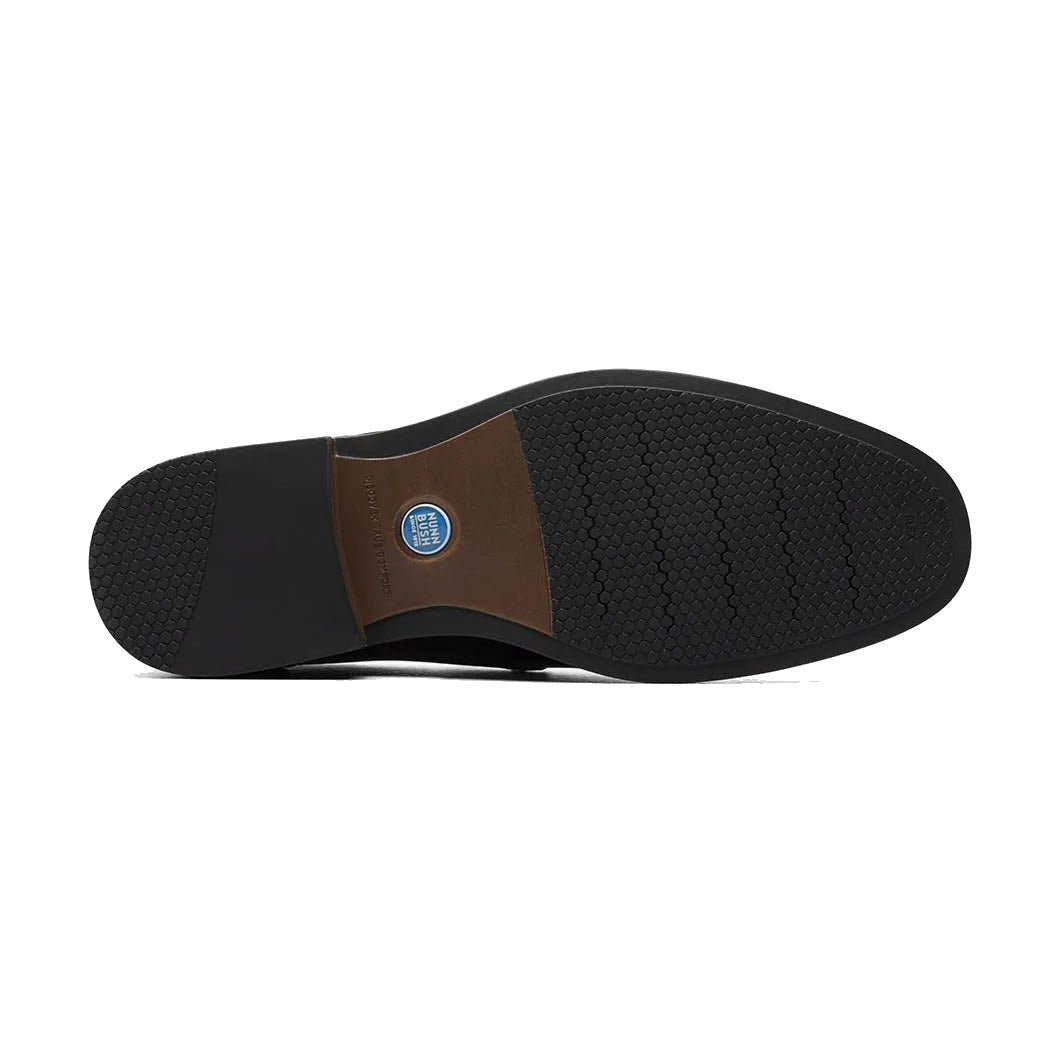 Sole of a shoe featuring a black Nunn Bush Centro Flex Moc Toe Venetian treading, a brown leather patch in the middle, and a circular blue logo.