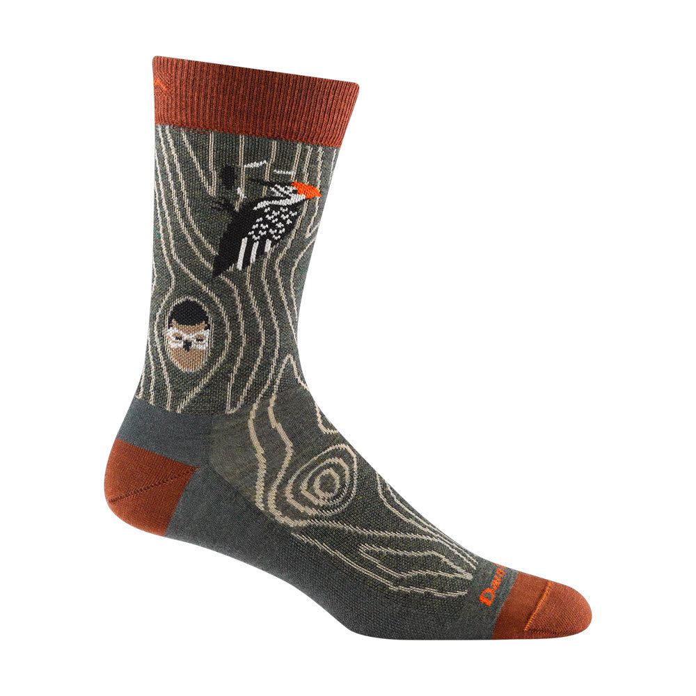 A Darn Tough Woody Crew Sock featuring an outdoor motif with patterns of trees and a small embroidered woodpecker on a green and brown background.