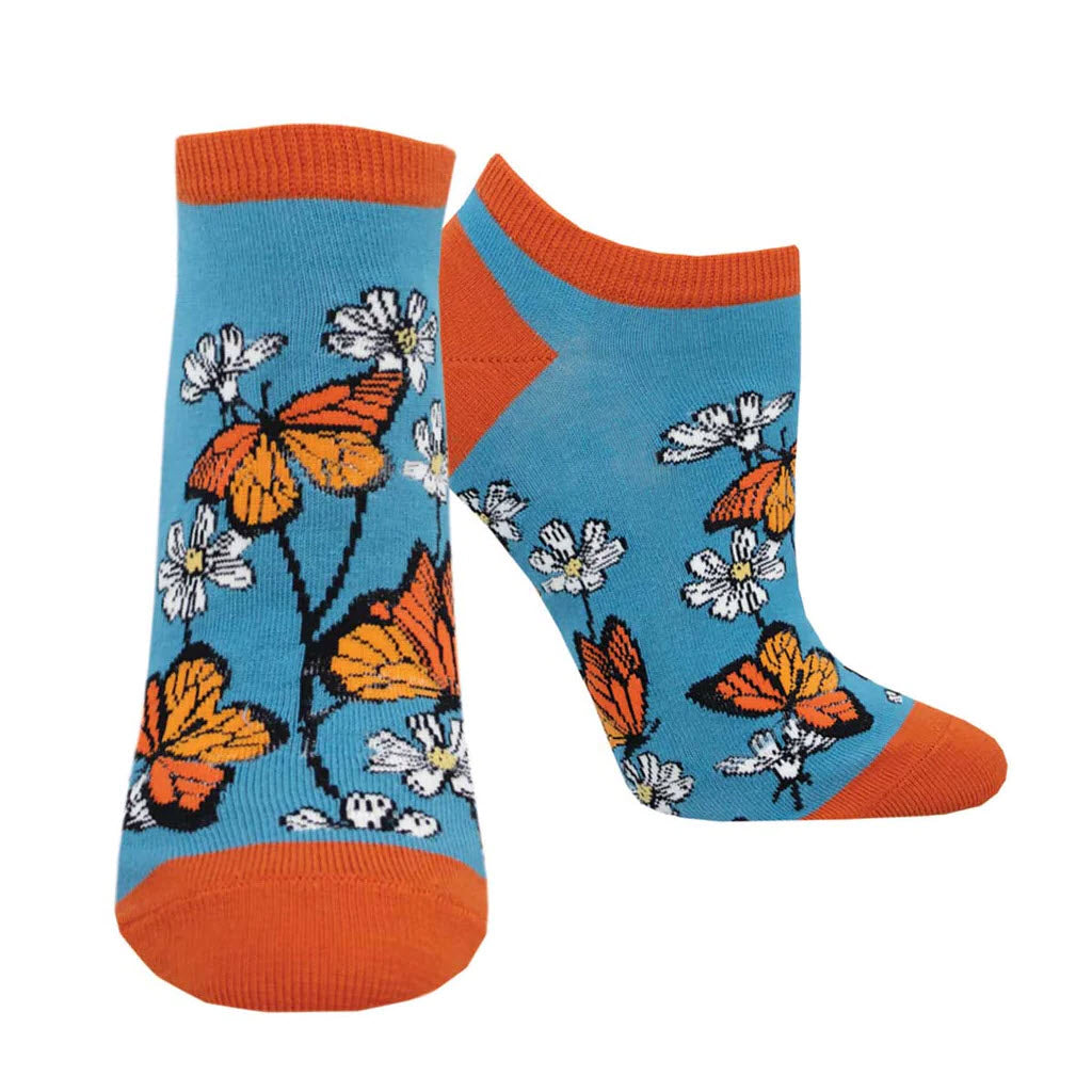 A pair of SOCKSMITH SHORTIE SOCKS DAISY MONARCH BLUE - WOMENS with an orange toe, heel, and cuff, featuring a pattern of orange butterflies and black-and-white flowers to brighten your drawer.