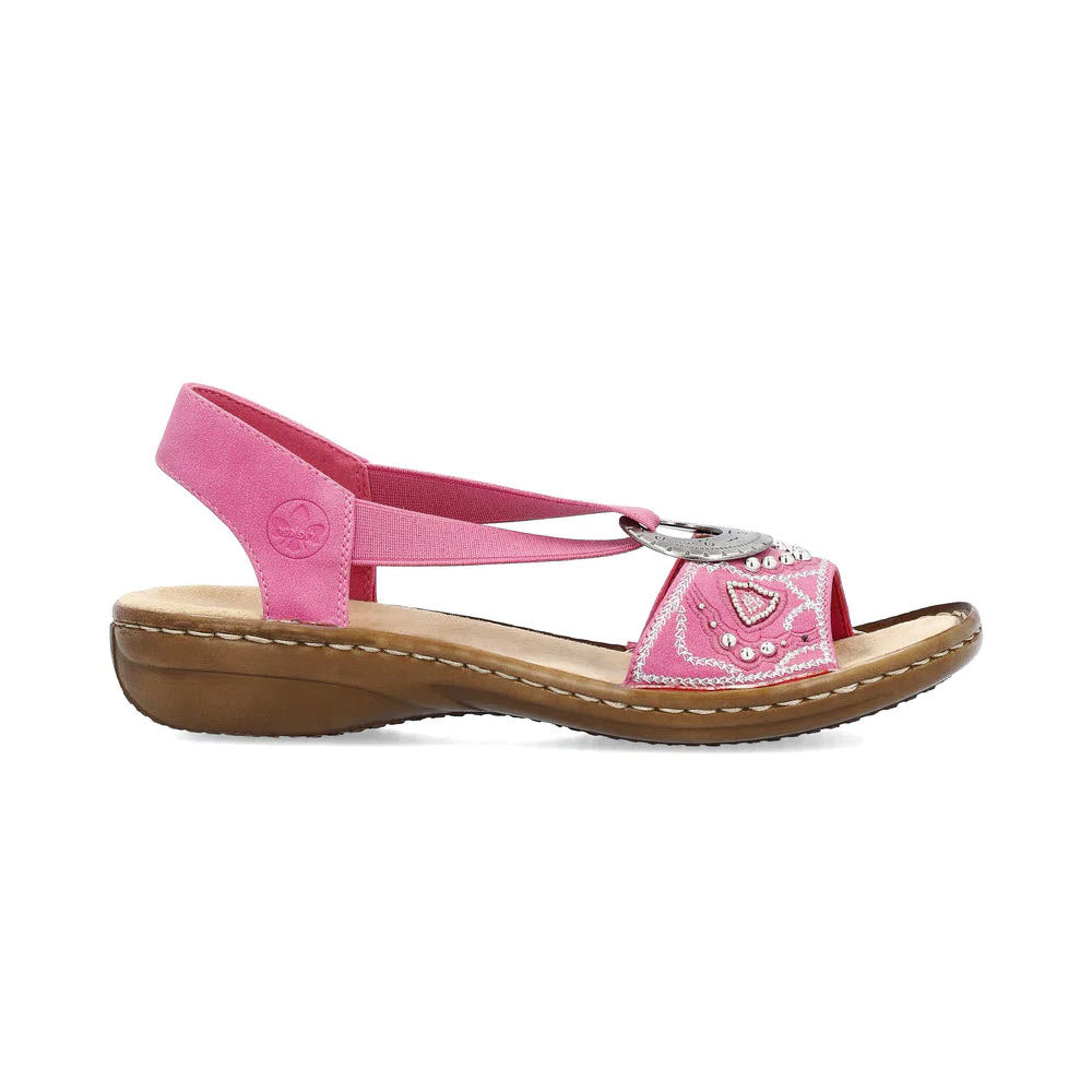 A Rieker pink sling-back sandal with a strap around the heel, decorative embroidery on the forefoot, and a buckle closure, set against a white background.