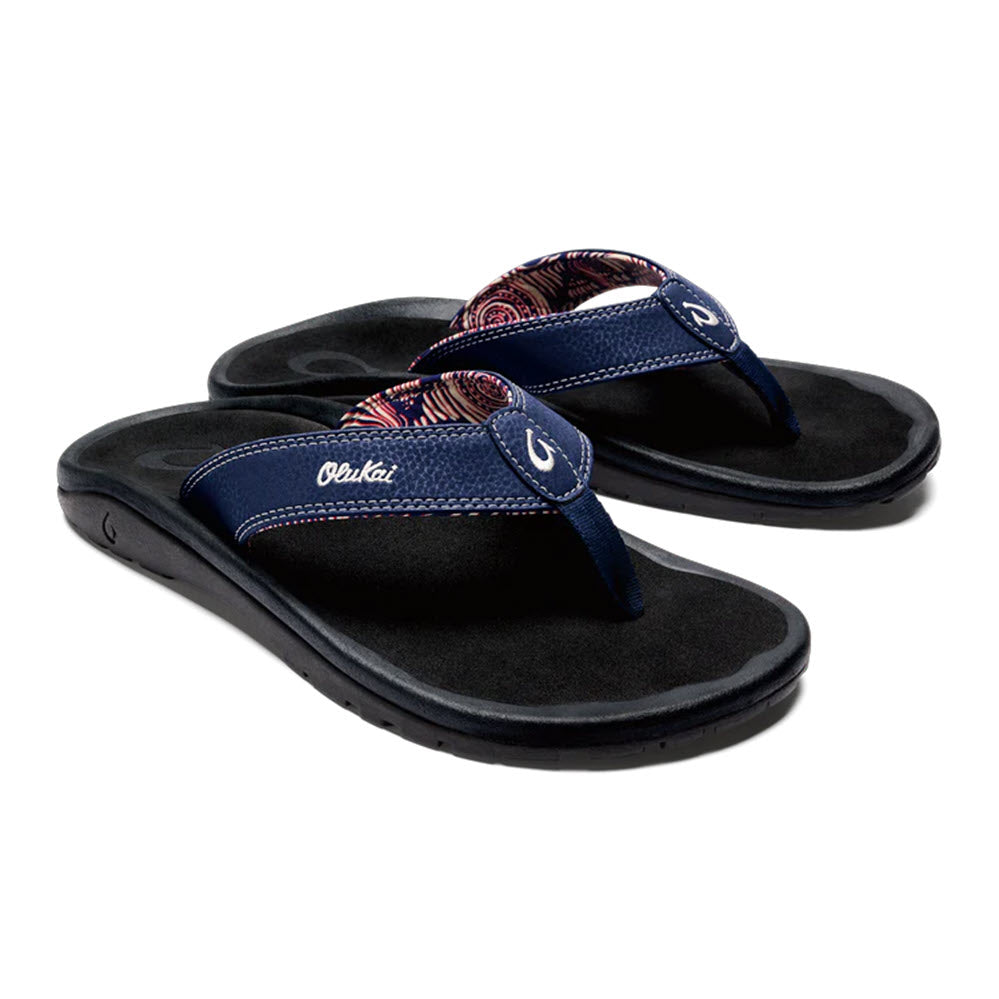 A pair of Olukai Ohana flip-flops with a non-slip EVA footbed, black sole, and a blue strap featuring a red and navy pattern.